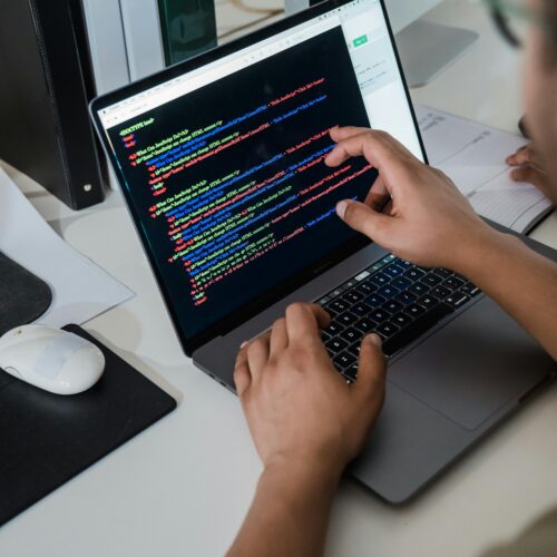 Close-up of a programmer pointing at a colorful code script on a laptop in an office setting.